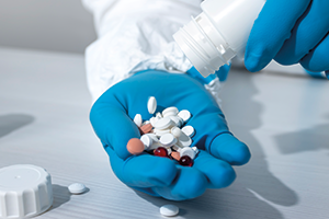 person wearing blue gloves pouring tablets onto their hand. Credit: AVAKAphoto