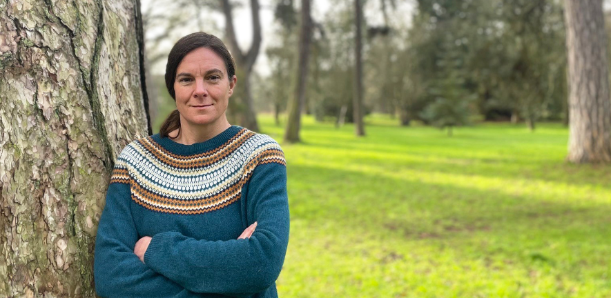 Katharina Schiessl Katharina Schiessl, smiling, arms crossed, wearing blue jumper, against a tree in the botanic gardens